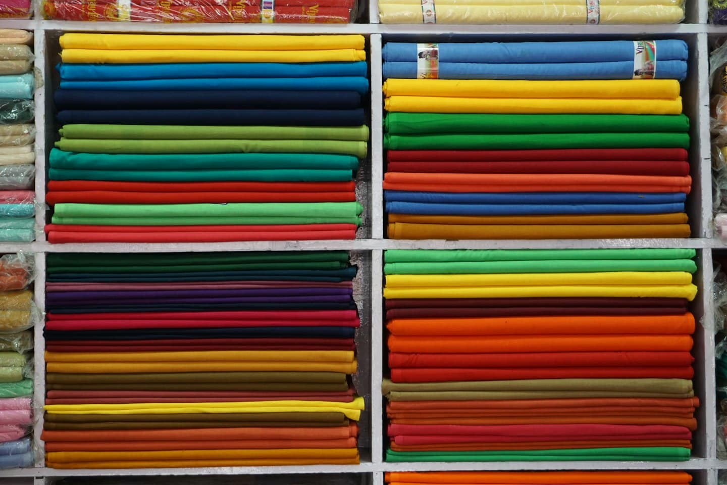 Pile di rotoli di stoffa colorata disposti sugli scaffali di legno di un negozio.
