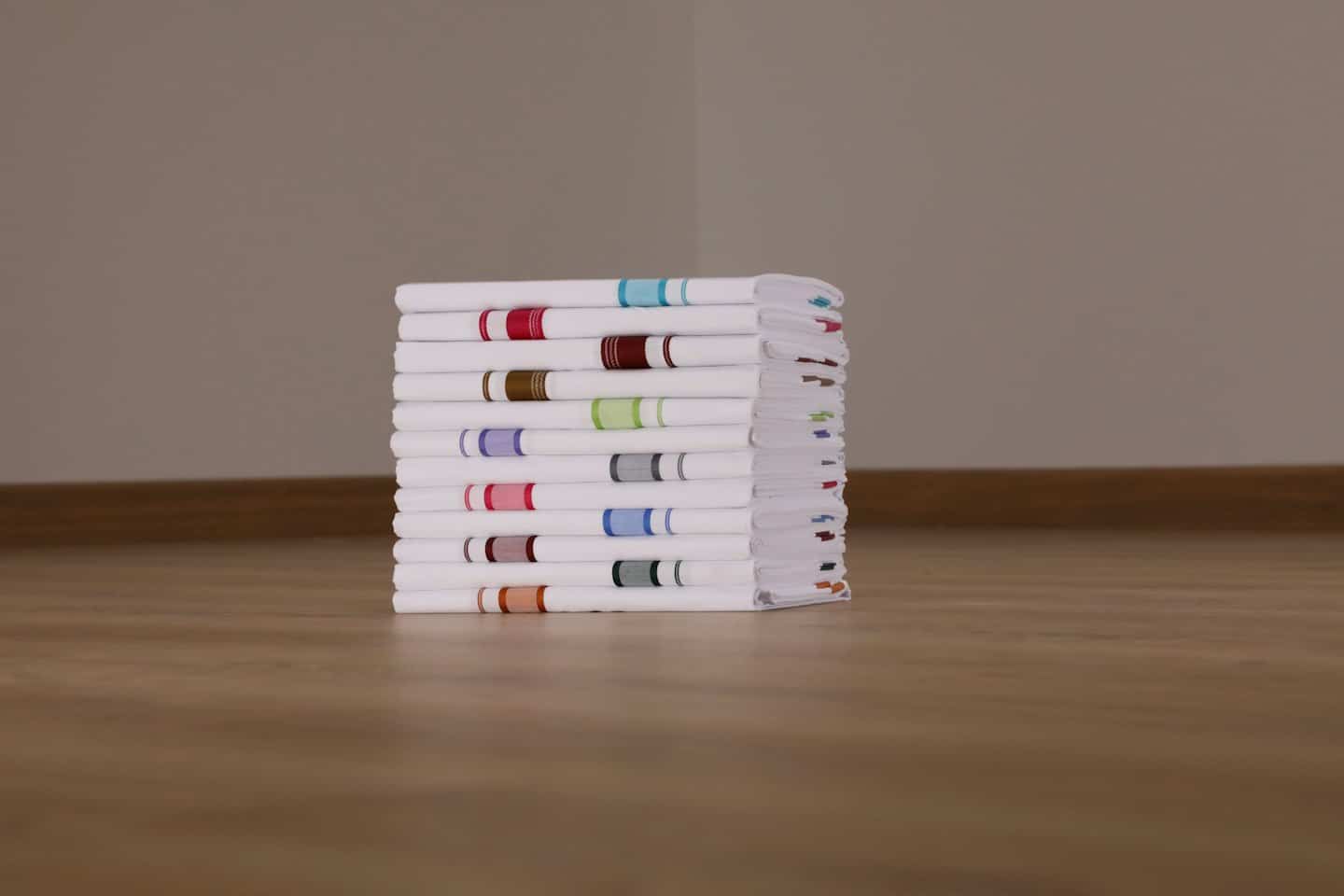 A stack of neatly folded white towels with colorful striped borders.